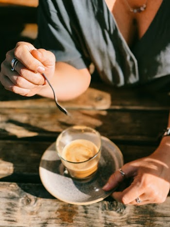 Person About to Stir Brown Liquid on Clear Glass Mug