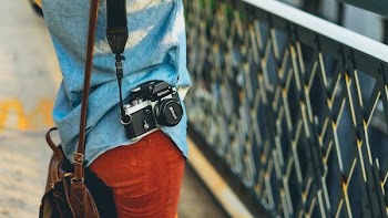person carrying bag and camera facing fence