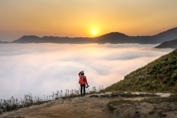 Person Carrying Red Backpack Facing Sea of Clouds