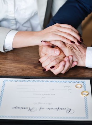 person clasp hands beside marriage certificate and wedding bonds