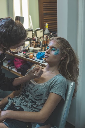 Person Doing Face Paitning on Woman Sittin on Teal Chair