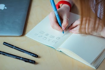 Person Drawing on Notebook Using Pen