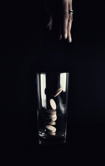Person Drop Tablets on Clear Drinking Glass on Black Surface