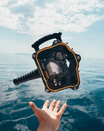 Person Grabbing Black and Orange Plastic Case Front of Calm Water