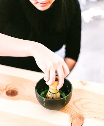 Person Holding a Bamboo Whisk in a Black Bowl Close-up Photography