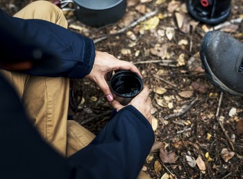 Person Holding Black and Gray Travel Mug With Sitting on Ground