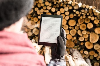 Person Holding Black E-book Reader Near Pile of Firewood