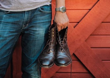 person holding black leather boots beside red barn door panel