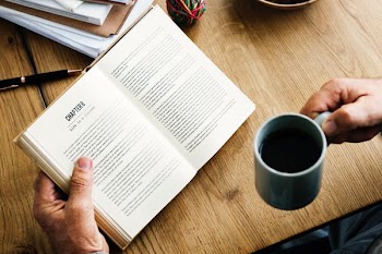 person holding blue mug and book near table