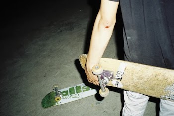 Person Holding Brown Skateboard Beside White and Green Skateboard