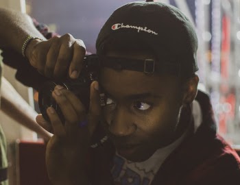 Person Holding Camera Wearing Black Champion Cap