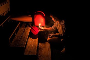 person holding candle lighting the red and black metal part in dark room near ladder