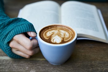 Person Holding Coffee Mug Beside Book