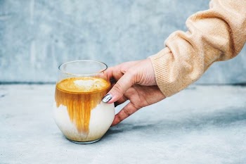 person holding cup filled with brown and white liquid