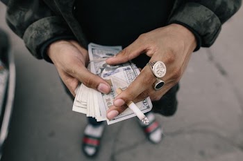 person holding dollar banknotes while pinning cigarette stick