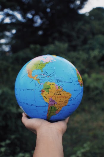 Person holding Earth globe in hand against green trees