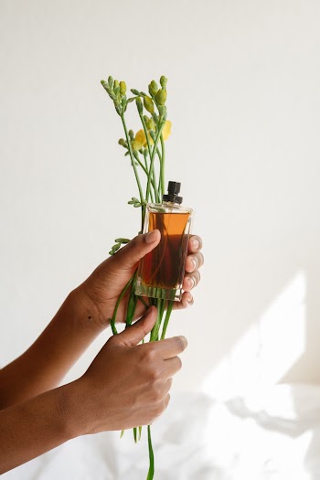 Person Holding Fragrance Bottle and Petaled Flower
