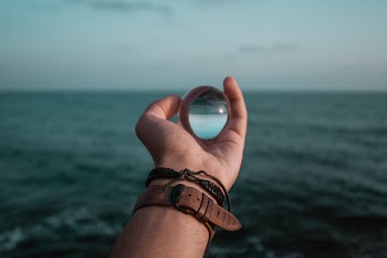 Person Holding Glass Marble Infront of Sea