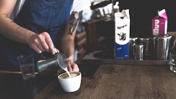person holding gray pitcher and teacup standing beside table