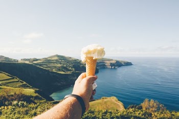 person holding ice cream with cone near body of water during daytime