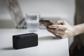 Person Holding Iphone Beside Black Portable Speaker