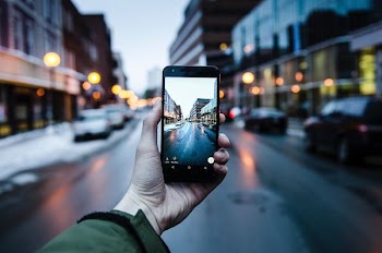 person holding iPhone while taking photo of asphalt road