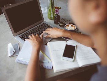 person holding MacBook Air beside phone on open book and notes