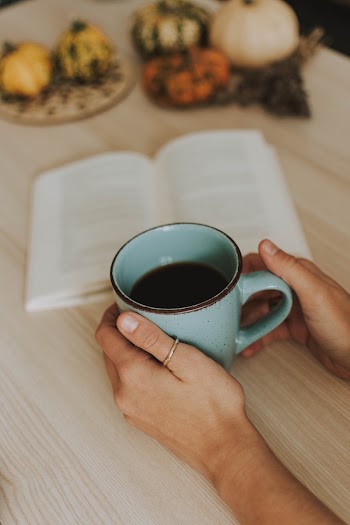 Person Holding Mug of Coffee Beside an Open Book