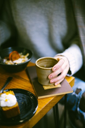 Person Holding Mug on Top of Brown Book
