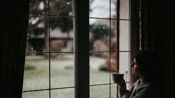 person holding mug while looking at window