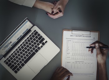 Person Holding Pen Writing on Daily Report Schedule Paper