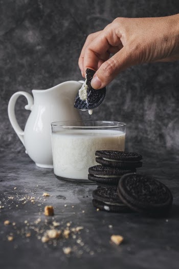 Person Holding Piece of Biscuit With Milk in Glass