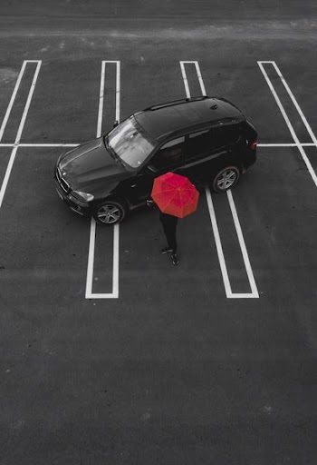 person holding red umbrella standing near black SUV