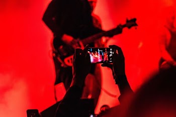 person holding smartphone in front of a person playing guitar on stage