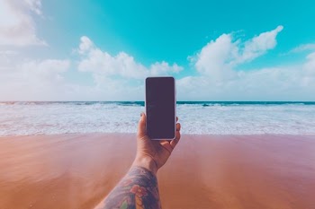 person holding smartphone near shore outdoors during daytime