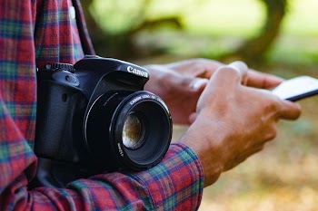 person holding smartphone with black Canon bridge camera on wrist at daytime