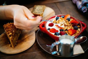Person Holding Spoon and Round Red Ceramic Bowl With Pastries