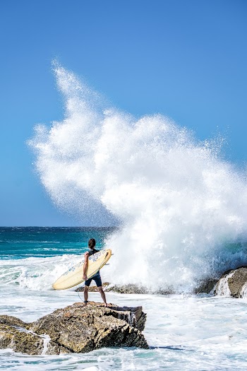 Person Holding Surfboard Standing On Rock 