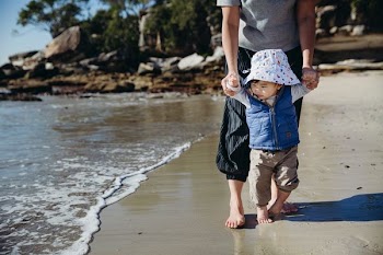 person holding toddler walking on beach at daytime