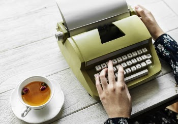 Person Holding Type Writer Beside Teacup and Saucer on Table