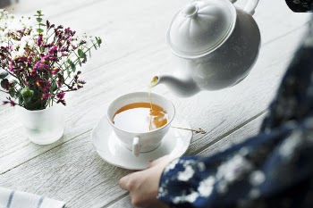 Person Holding White Ceramic Teapot and Pouring Tea in Cup