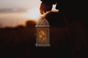 person holding white metal framed clear glass lantern during golden hour
