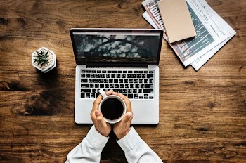 person holding white mug over MacBook Pro