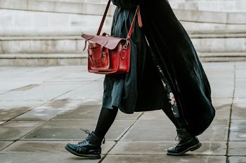 person in black coat carrying satchel bag while walking on street