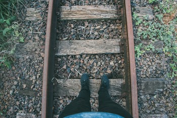 Person in Black Fitted Jeans and Sneakers Stepping on Wooden Trail Way