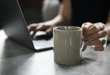 Person in Black Top Holding White Ceramic Mug and Using Laptop Computer