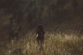person in black top surrounded by bushes with trees ahead during daytime