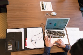 Person in Blue Dress Shirt Facing White Laptop on Brown Wooden Table