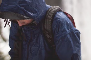 person in blue raincoat and black backpack walking with head low