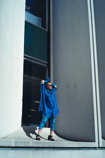Person in Blue Top and Blue Pedal Short Standing by the Building Glass Window